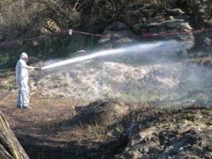 Boeing worker shoots a load of water over the debris field to keep asbestos dust down.